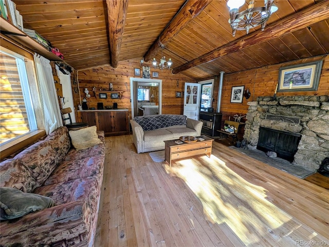 living room featuring vaulted ceiling with beams, a stone fireplace, and wooden walls