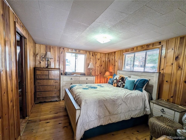 bedroom featuring multiple windows, wood walls, and light hardwood / wood-style flooring