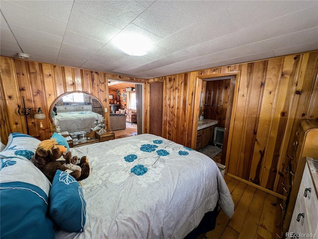 bedroom with connected bathroom, radiator, wood walls, and hardwood / wood-style floors