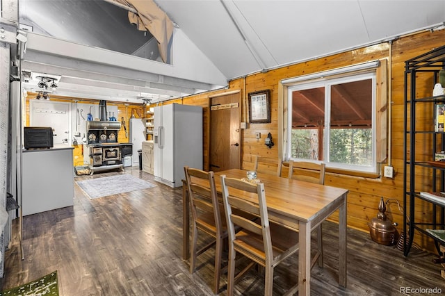 dining room featuring dark hardwood / wood-style flooring, wooden walls, and vaulted ceiling