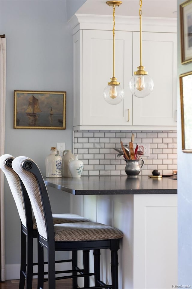 10886 E Berry Ave, Englewood, CO 80111 - kitchen featuring decorative backsplash, a kitchen breakfast bar, white cabinetry, dark countertops, and pendant lighting