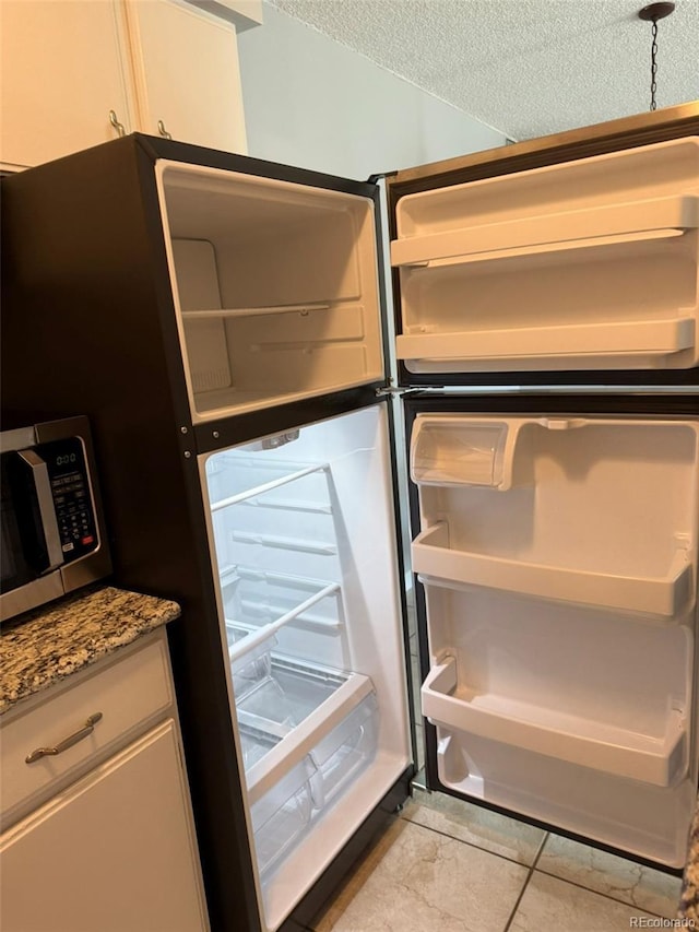 kitchen view of refrigerator, stainless steel microwave, a textured ceiling, and stone countertops