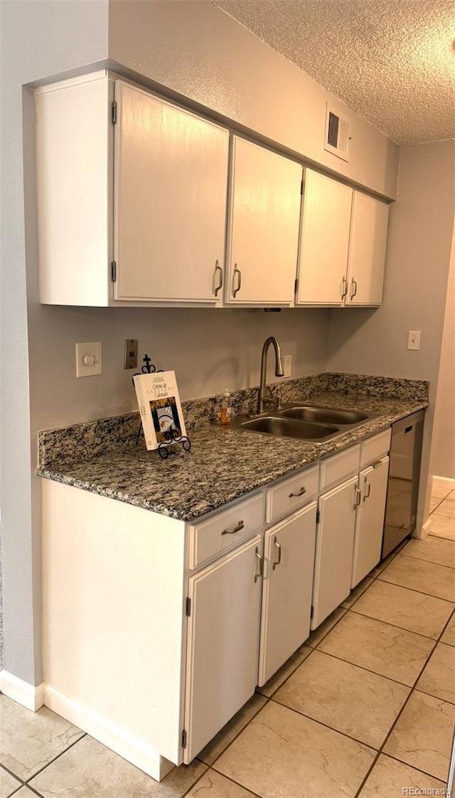 kitchen with a sink, a textured ceiling, dishwasher, light tile patterned floors, and baseboards