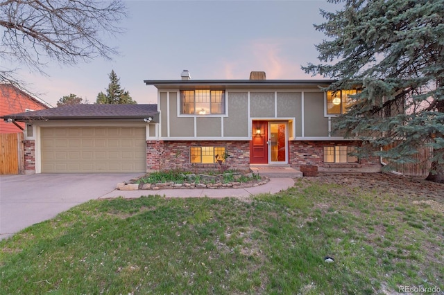 bi-level home featuring brick siding, concrete driveway, a garage, stucco siding, and a lawn