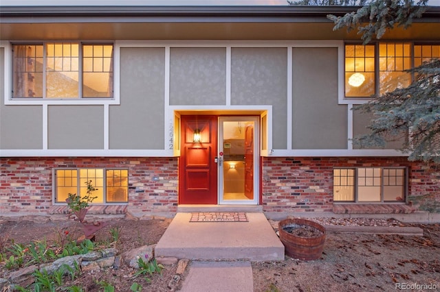view of exterior entry with stucco siding and brick siding