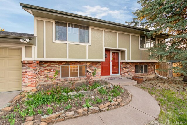 bi-level home with stucco siding, brick siding, and a garage