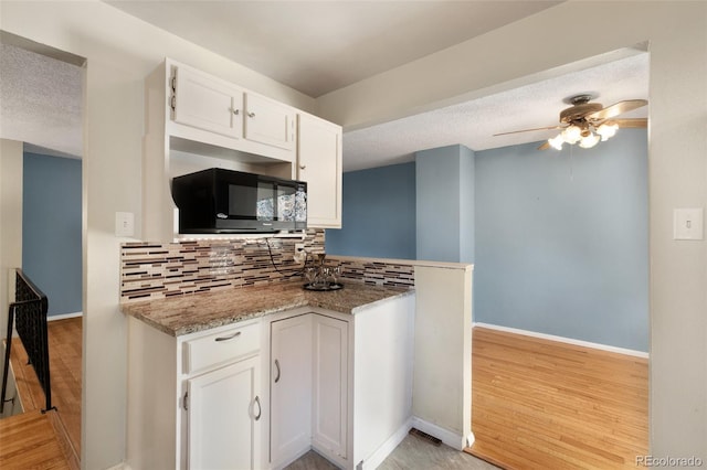 kitchen with a ceiling fan, white cabinets, light wood-type flooring, backsplash, and black microwave