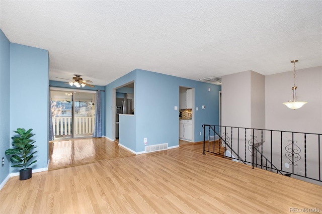 empty room with wood finished floors, a textured ceiling, visible vents, baseboards, and ceiling fan