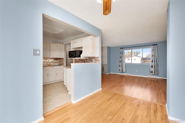 kitchen with black microwave, light wood finished floors, white cabinets, and decorative backsplash