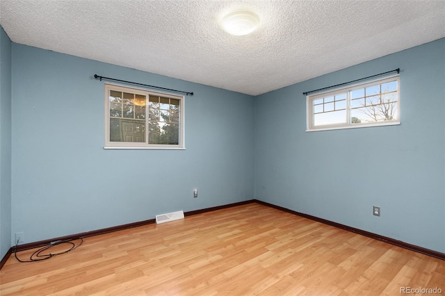 empty room with baseboards, light wood-style floors, visible vents, and a textured ceiling