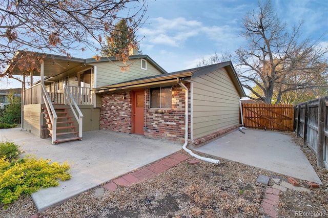back of house with stairway, a patio, brick siding, and fence