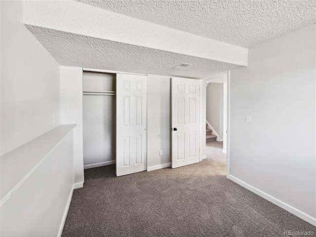 unfurnished bedroom with baseboards, a closet, dark carpet, and a textured ceiling