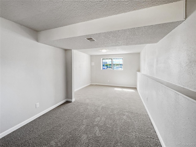 basement featuring carpet, visible vents, a textured ceiling, and baseboards