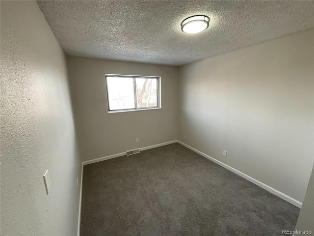 empty room with a textured ceiling, dark colored carpet, visible vents, and baseboards