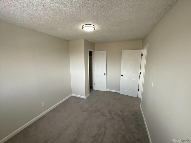 unfurnished bedroom with dark colored carpet, a textured ceiling, and baseboards