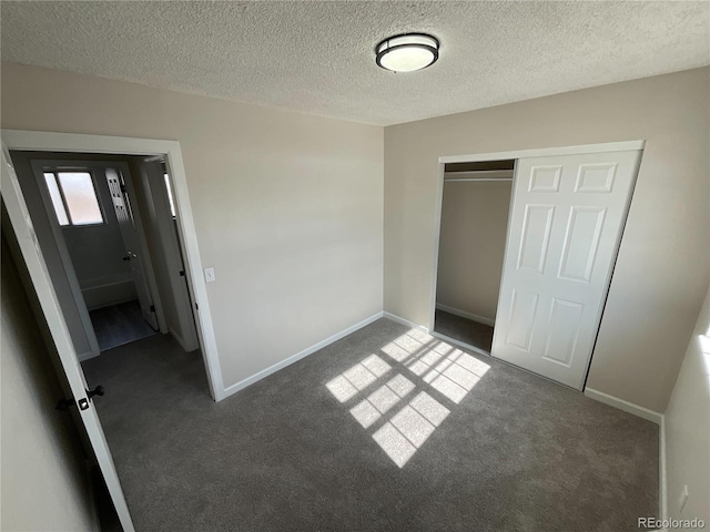 unfurnished bedroom featuring a textured ceiling, a closet, dark carpet, and baseboards