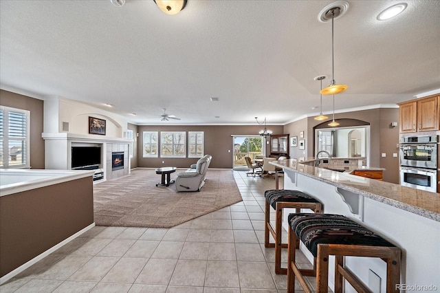 interior space featuring double oven, open floor plan, light stone countertops, a tiled fireplace, and pendant lighting