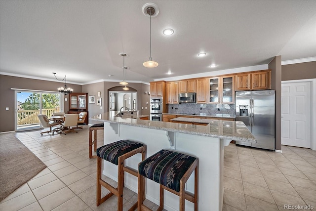 kitchen with light stone counters, pendant lighting, brown cabinets, stainless steel appliances, and glass insert cabinets