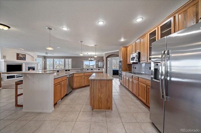 kitchen featuring open floor plan, hanging light fixtures, appliances with stainless steel finishes, a center island, and glass insert cabinets