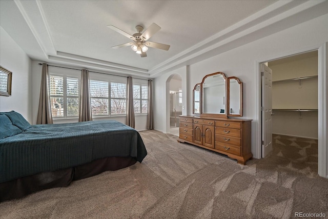 bedroom featuring arched walkways, a tray ceiling, carpet, a spacious closet, and ceiling fan