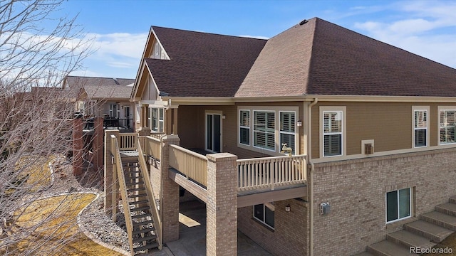 rear view of property featuring a balcony, roof with shingles, stairway, and brick siding