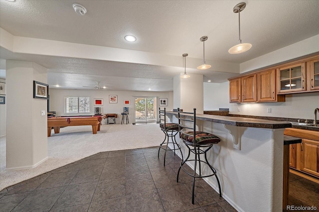 kitchen featuring glass insert cabinets, open floor plan, dark colored carpet, a kitchen bar, and pendant lighting