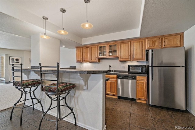 kitchen with stainless steel appliances, brown cabinets, dark countertops, a kitchen bar, and glass insert cabinets