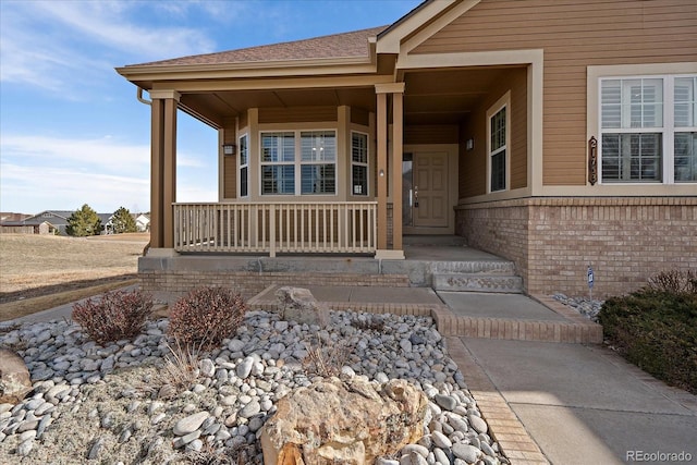 entrance to property with brick siding, roof with shingles, and a porch