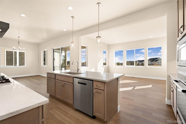 kitchen with sink, hanging light fixtures, stainless steel appliances, and an island with sink