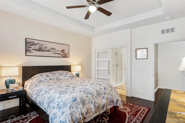 bedroom with connected bathroom, a tray ceiling, ceiling fan, and dark wood-type flooring