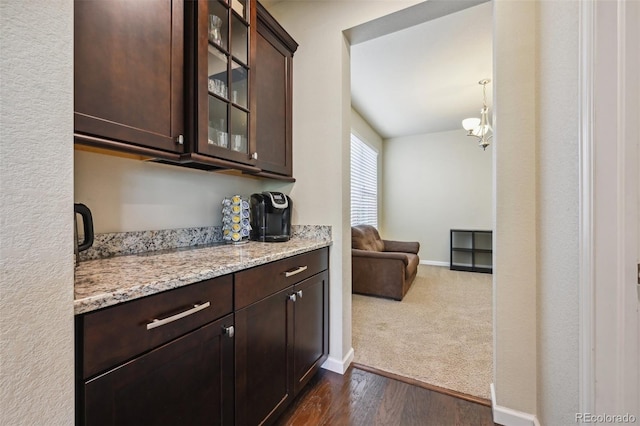 bar with dark brown cabinetry, dark wood-type flooring, pendant lighting, and light stone counters