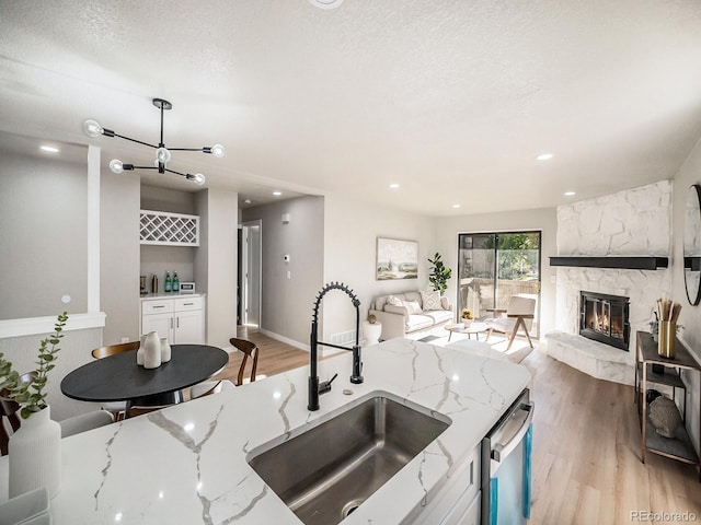 kitchen featuring a fireplace, a textured ceiling, light hardwood / wood-style flooring, light stone counters, and sink