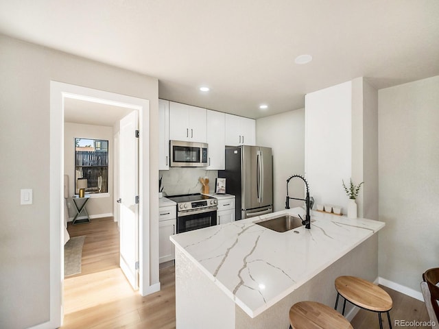 kitchen with kitchen peninsula, sink, white cabinetry, appliances with stainless steel finishes, and light stone counters