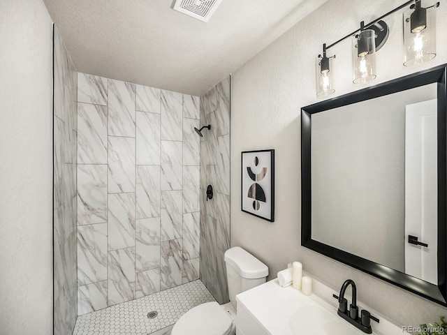 bathroom with a textured ceiling, toilet, vanity, and a tile shower