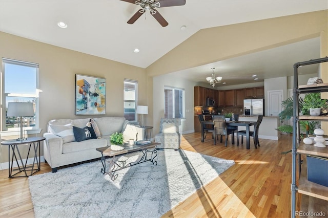 living room with ceiling fan with notable chandelier, light wood-type flooring, and vaulted ceiling