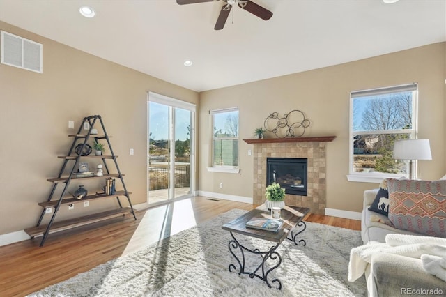 living room featuring a tile fireplace, ceiling fan, and light hardwood / wood-style floors