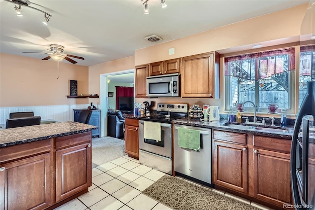 kitchen featuring dark stone counters, stainless steel appliances, ceiling fan, sink, and light tile patterned floors