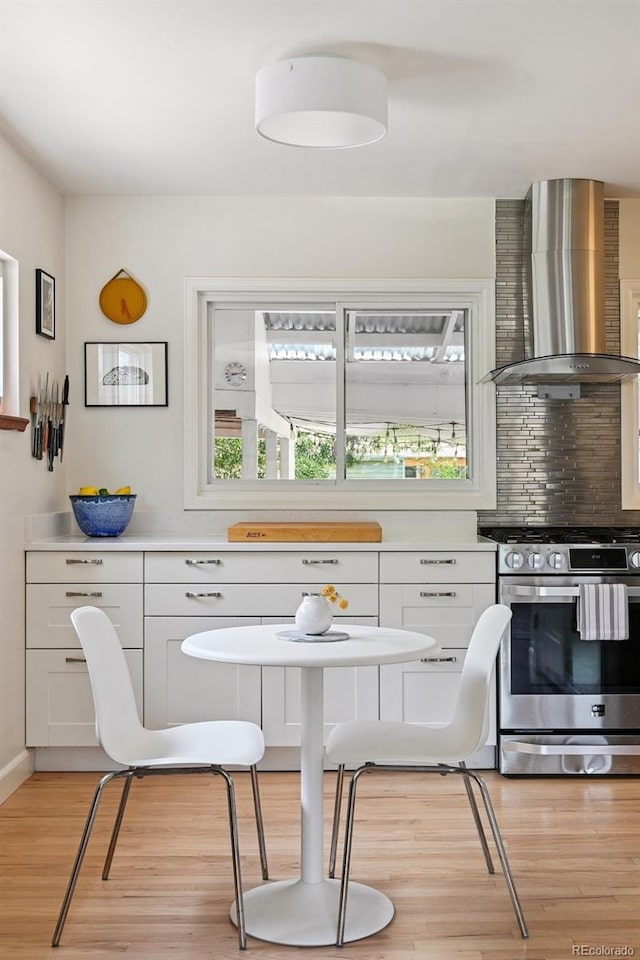 2965 S Gilpin St, Denver, CO 80210 - kitchen with wall chimney range hood, stainless steel range with gas cooktop, light wood finished floors, light countertops, and white cabinetry