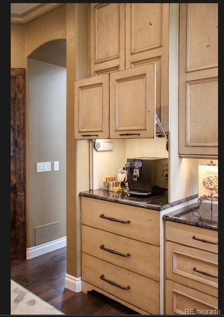 kitchen with visible vents, baseboards, arched walkways, light brown cabinetry, and dark wood-type flooring