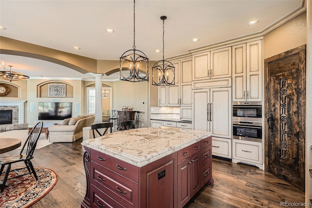 kitchen with open floor plan, decorative columns, stainless steel oven, cream cabinetry, and paneled refrigerator