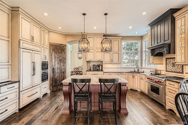 kitchen with backsplash, a center island, high quality appliances, arched walkways, and a sink