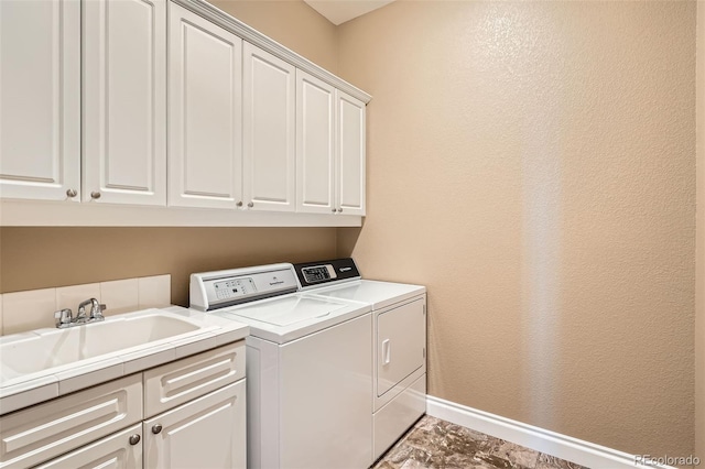 washroom with a sink, baseboards, cabinet space, and washer and clothes dryer