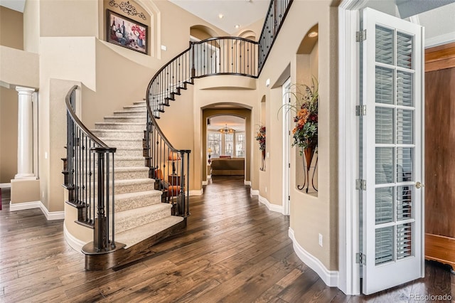 entryway with dark wood-style floors, arched walkways, ornate columns, and a towering ceiling