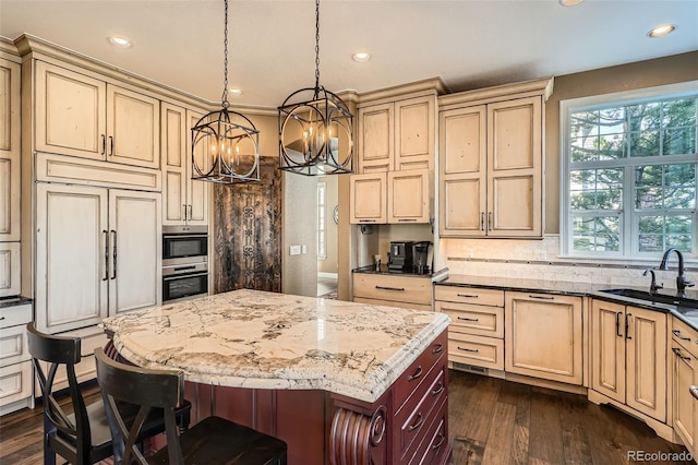 kitchen with a sink, a kitchen breakfast bar, cream cabinets, backsplash, and paneled built in fridge