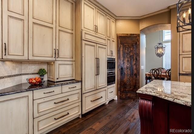 kitchen with dark stone counters, arched walkways, cream cabinetry, and dark wood-style floors