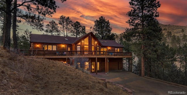 back of property at dusk with a wooden deck, driveway, and an attached garage