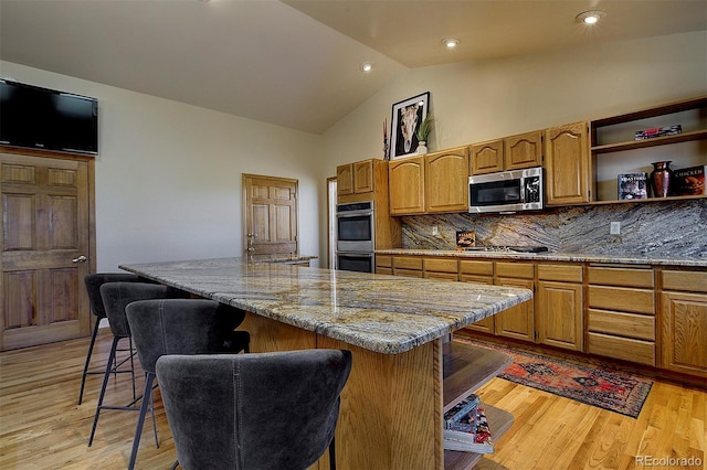 kitchen featuring light wood finished floors, backsplash, a center island, a kitchen bar, and appliances with stainless steel finishes