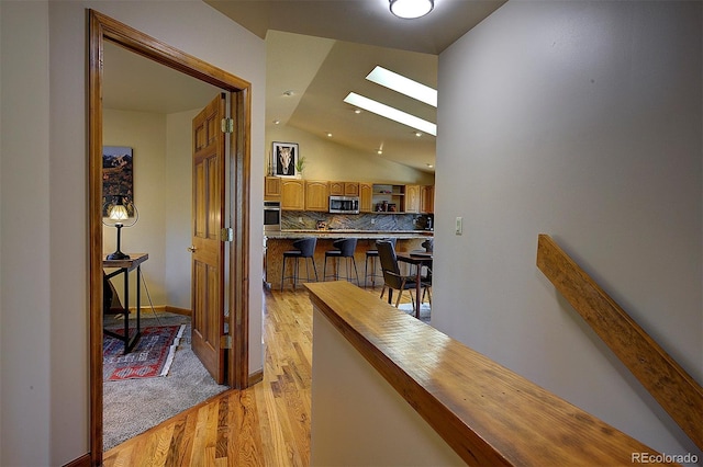 hallway with vaulted ceiling with skylight and light wood-style flooring