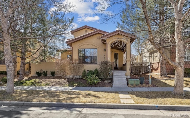 mediterranean / spanish home featuring a fenced front yard, stucco siding, and a tiled roof