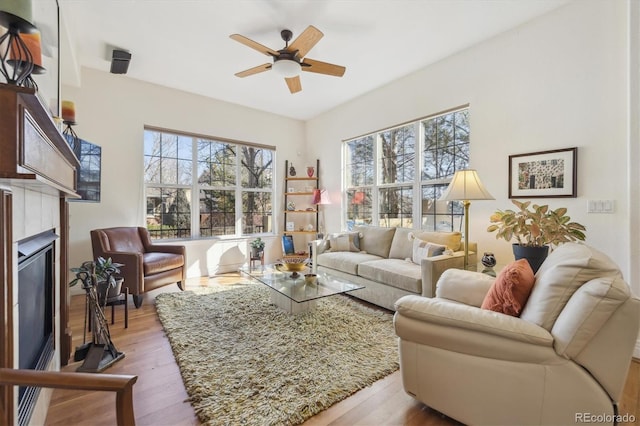 living room featuring a wealth of natural light, a glass covered fireplace, a ceiling fan, and wood finished floors